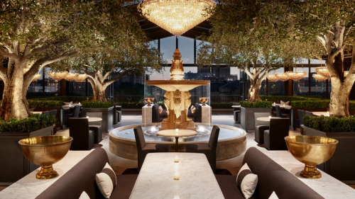 Elegant restaurant interior featuring a central fountain, lush greenery, and chandeliers, creating a warm ambiance.