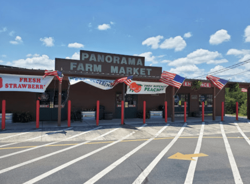 Exterior of Panorama Farm Market with banners for fresh strawberries and peaches, and American flags, under a blue sky.