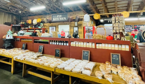 A cozy pie kitchen with shelves of baked goods, jars, and a rustic wooden counter in a warm, inviting setting.