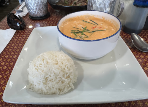 A bowl of creamy soup with shrimp and herbs, served alongside a mound of white rice on a decorative plate.