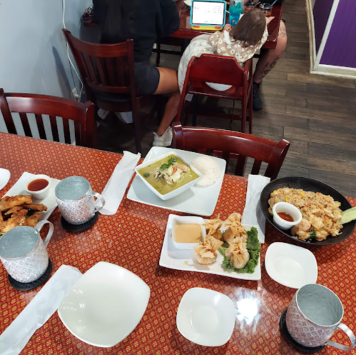 A table set with various dishes, including fried chicken, rice, and a green curry, in a casual dining setting.