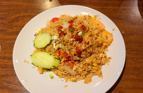 A plate of fried rice topped with shrimp, vegetables, and garnished with cucumber slices.