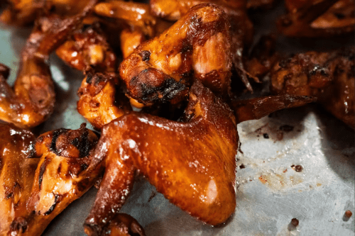 Close-up of crispy, glazed chicken wings on a metal tray, showcasing a rich, golden-brown color.