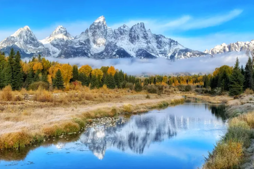 A serene landscape featuring snow-capped mountains, autumn trees, and a reflective river under a clear blue sky.