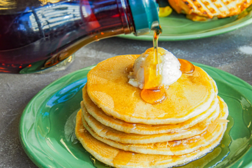 A stack of pancakes topped with a dollop of butter and syrup being poured over them on a green plate.