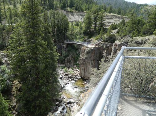 A scenic view of a rocky gorge with a bridge, surrounded by lush green trees and a flowing river below.