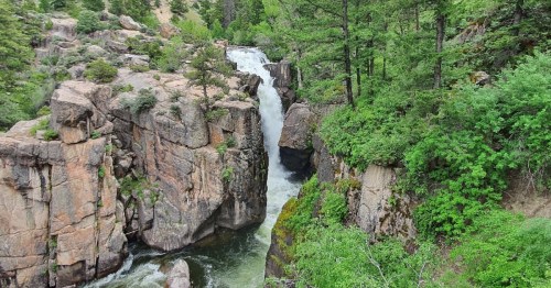 A scenic waterfall cascading between rocky cliffs, surrounded by lush green trees and vegetation.