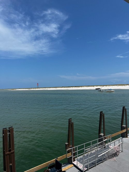 A serene view of a calm waterway with a sandy shore and a boat in the distance under a clear blue sky.