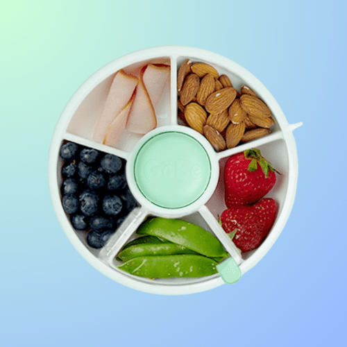 A divided snack container with turkey slices, almonds, blueberries, strawberries, and sugar snap peas on a gradient background.