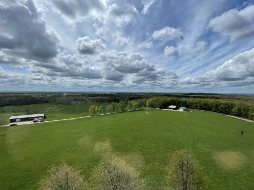 A panoramic view of a green field with trees, a barn, and a cloudy sky in the background.