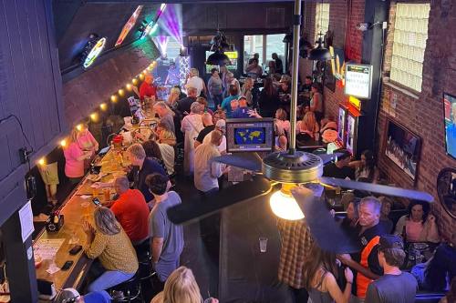 A lively bar scene with a crowded atmosphere, colorful lights, and people socializing at the bar and tables.