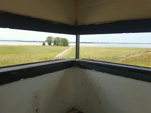 View from a corner window overlooking a grassy field, path, and a body of water in the distance.