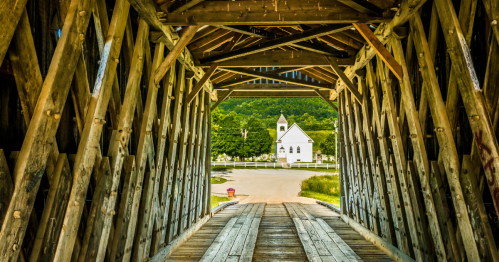 view of a small white church as seen through the wood-beam interior of the Goddard Covered Bridge in Kentucky