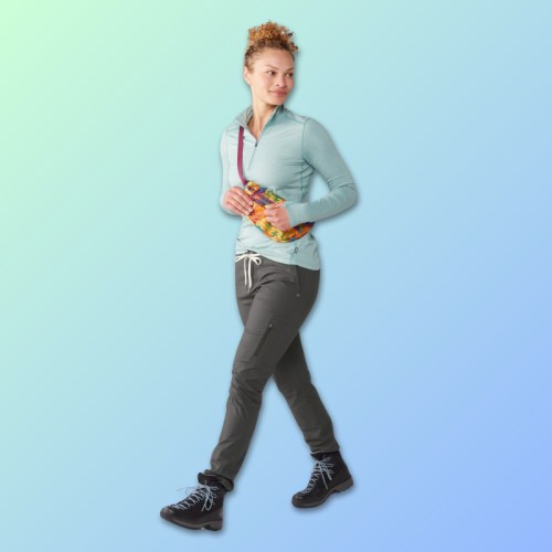 A woman in a light blue hoodie and gray pants walks confidently, holding a colorful bag, against a gradient background.