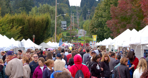 A large crowd of people walks along a stretch of vendors under white canopies.