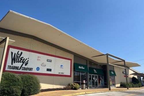 Exterior of Wiley's Trading Company building with a large sign, clear blue sky, and surrounding greenery.