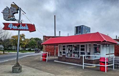 A small ice cream shop with a red roof and vintage sign, located on a quiet street under a cloudy sky.
