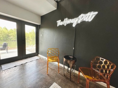 A cozy interior with two honeycomb-patterned chairs, a small table, and a neon sign reading "The Honey Pit."