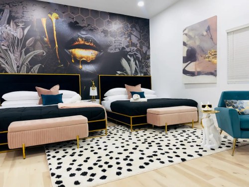 A stylish hotel room with two beds, a bold wall mural, and modern decor, featuring a plush rug and accent furniture.