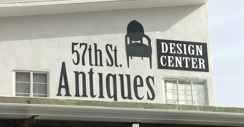 Sign for "57th St. Antiques" and "Design Center" on a white building. Features a chair graphic.