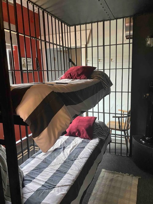 A small room with a bunk bed enclosed in bars, featuring red walls and simple furnishings.