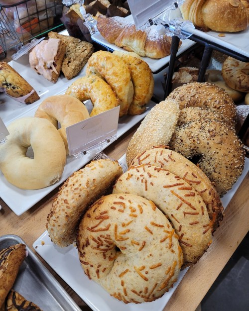 A variety of freshly baked bagels and pastries displayed on white plates in a bakery.