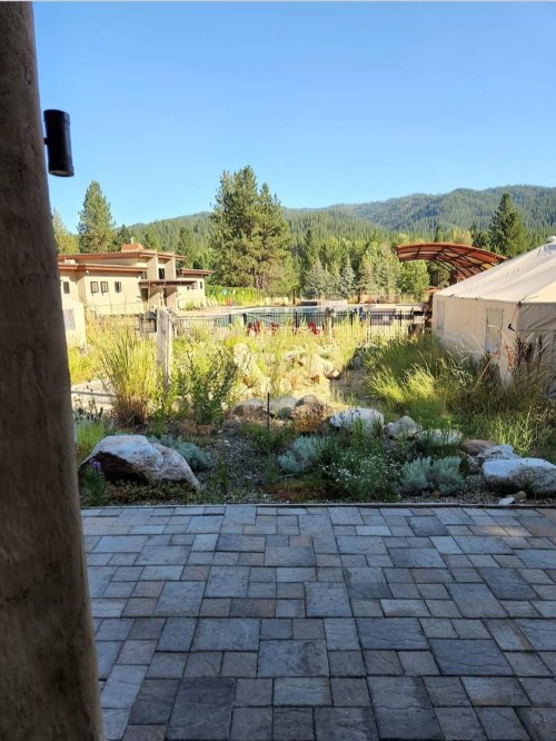 A scenic view of a garden with mountains in the background, framed by a stone pathway and rustic buildings.