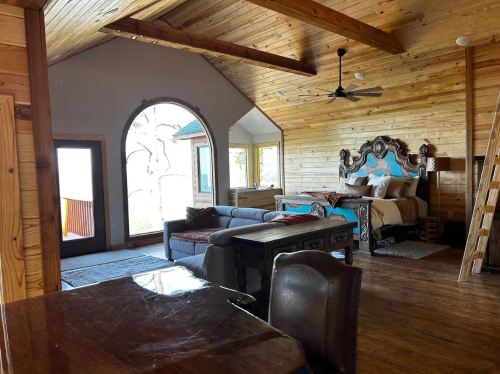 Cozy wooden interior of a spacious bedroom with a large bed, sofa, and arched window overlooking nature.