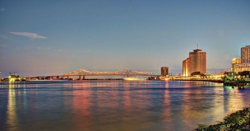 Views of New Orleans at sunset, with an illuminated bridge and buildings reflecting on the Mississippi.