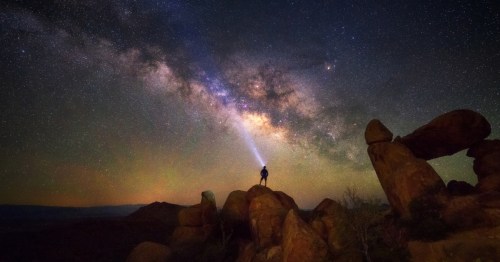 a stargazer stands on a boulder under the milky way at big bend national park in texas