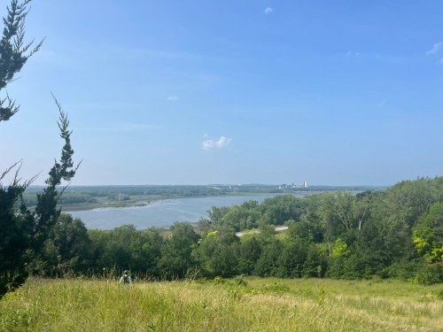A scenic view of a river surrounded by greenery under a clear blue sky, with distant buildings on the horizon.