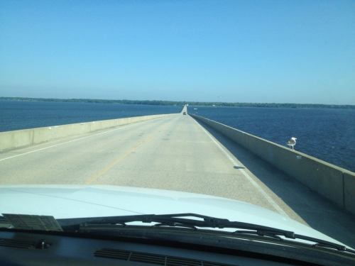 A view of a long, straight road extending over water under a clear blue sky.