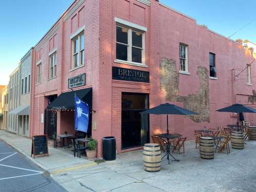 A pink building with "Bristol" signage, outdoor seating, and umbrellas on a quiet street.