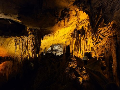 A dimly lit cave with dramatic rock formations and warm orange lighting, showcasing stalactites and stalagmites.