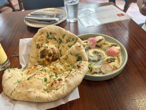 A plate with garlic naan and a dish of assorted appetizers, including pickled vegetables, on a wooden table.