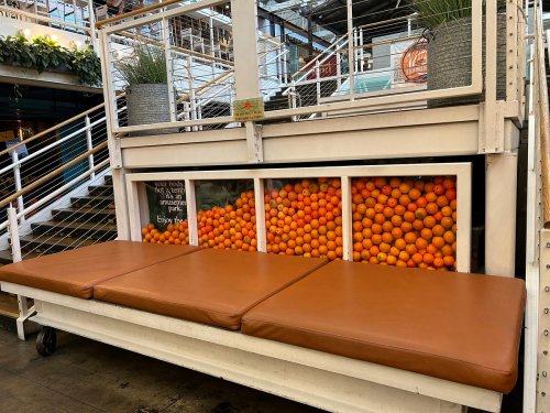 A cozy seating area with a brown cushion, showcasing a large display of oranges behind a glass panel.