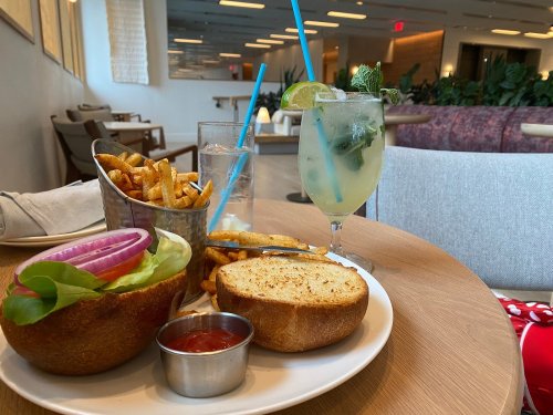 A plate with a burger, fries, and a drink with mint and lime, set in a modern restaurant interior.