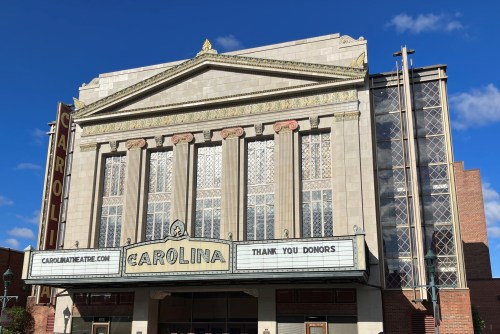 Historic Carolina Theatre building with a marquee thanking donors, under a clear blue sky.