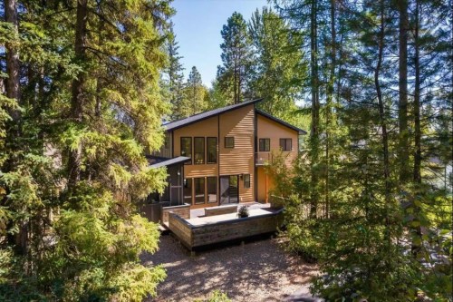 Modern house nestled among tall trees, featuring a deck and large windows, surrounded by lush greenery.