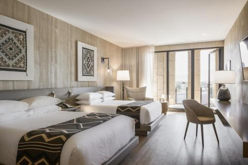 Modern hotel room with two beds, stylish decor, large windows, and a cozy seating area.