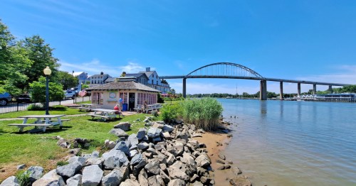 a canal-side restaurant with lawn seating and views of the cheasapeake city bridges in maryland on a sunny day
