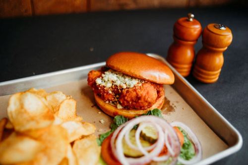A crispy chicken sandwich with toppings, served with potato chips and a side of lettuce, tomato, and pickles.