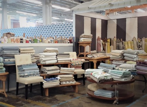 A display of neatly rolled fabrics and textiles on tables and shelves in a bright, spacious interior.