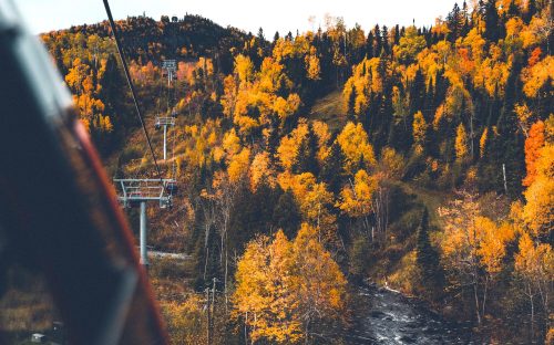 A scenic view from a cable car, showcasing vibrant autumn foliage and a winding river below.