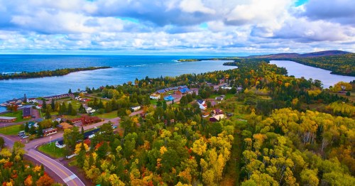Aerial view of a serene coastal village in Copper Harbor, Michigan with vibrant fall foliage and expansive Lake Superior.