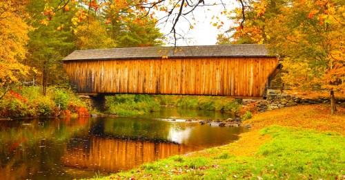 Sugar River flowing beneath historic Corbin wooden bridge in Newport, New Hampshire, with reflections and fall foliage on a rainy day.