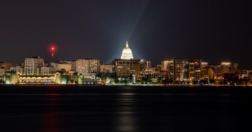 Night view of a city skyline featuring a prominent dome, illuminated buildings, and a calm water foreground.