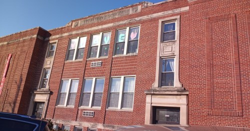 Brick building with large windows, decorated with colorful letters and hearts in the windows spelling "LOVE."