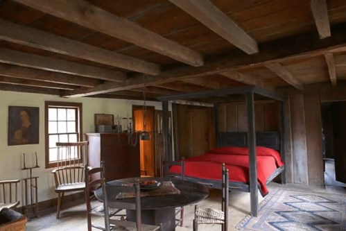 Cozy rustic room featuring a red bed, wooden furniture, and exposed beams, with a warm, inviting atmosphere.