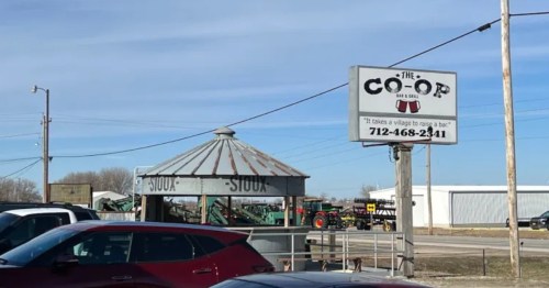 A rustic wooden sign for The Co-Op Bar and Grill next to a small gazebo in Pomeroy, Iowa.